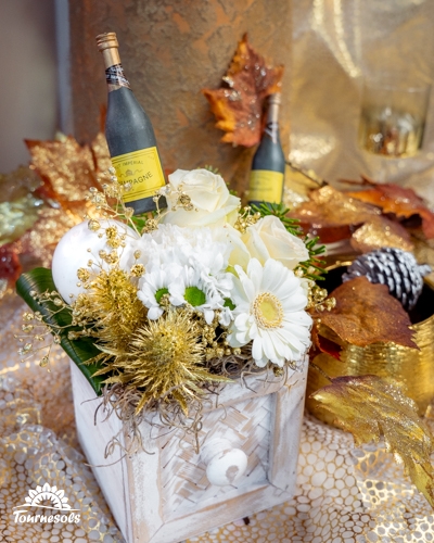 Composition florale du Nouvel An aux fleurs blanches et touches dorées, avec mini bouteilles de champagne.